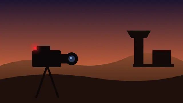 Silhouette of a broadcast camera with a red recording light against desert dunes at dusk